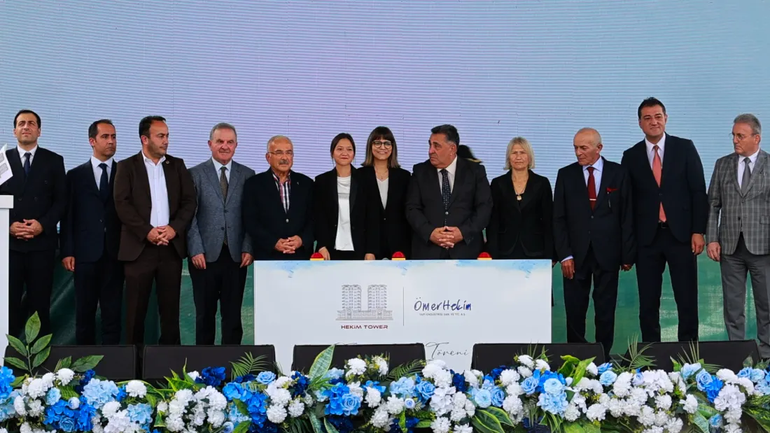 Temel atma anı: protokol, önlerinde Hekim Tower ve Ömer Hekim Yapı künyeli pano, sahne önü mavi ve beyaz çiçeklerle donatılmış