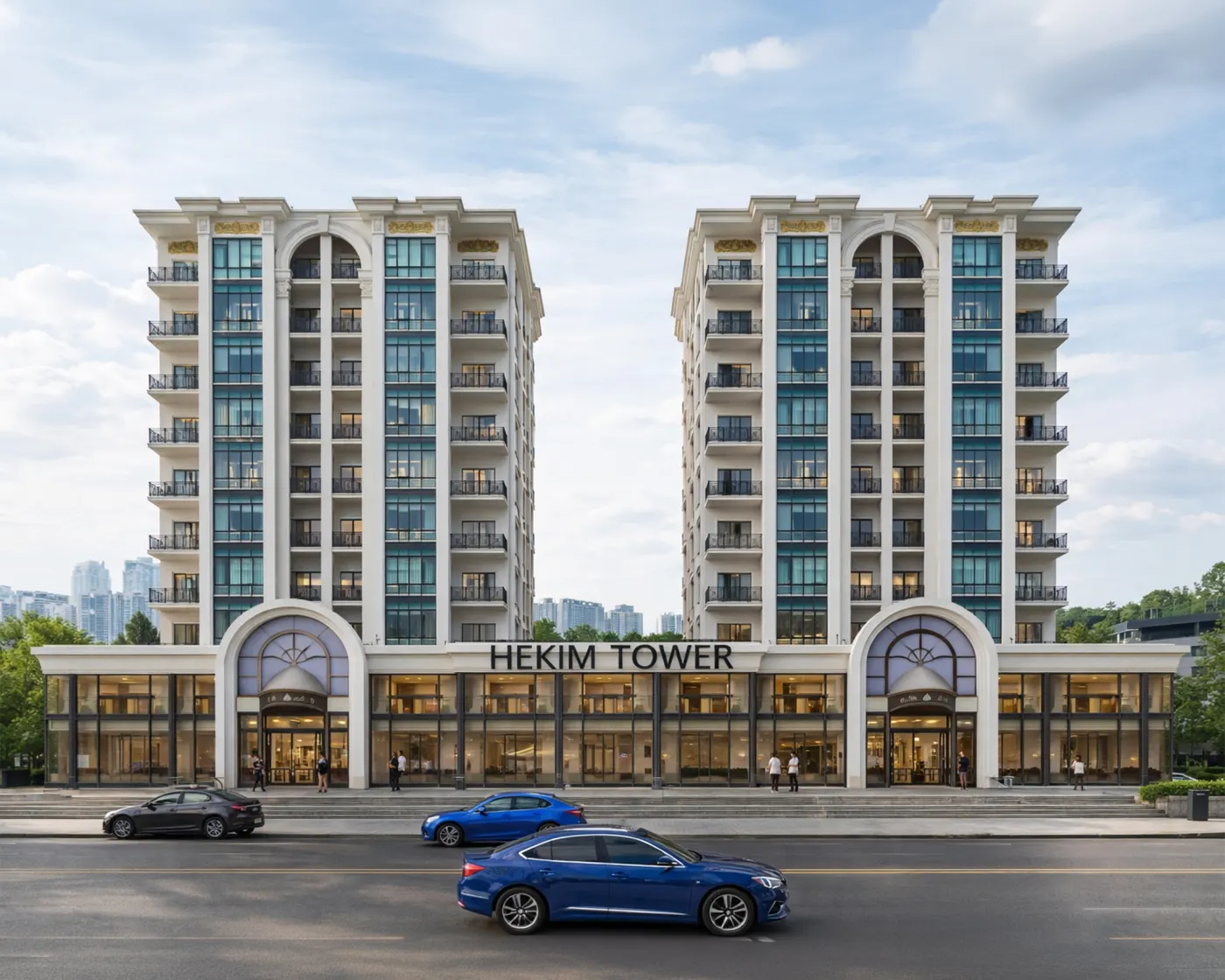 Hekim Tower'ın cadde tarafından görünümü: iki beyaz kule, kemerli girişler ve aydınlatılmış vitrinli zemin kat ticari birimleri