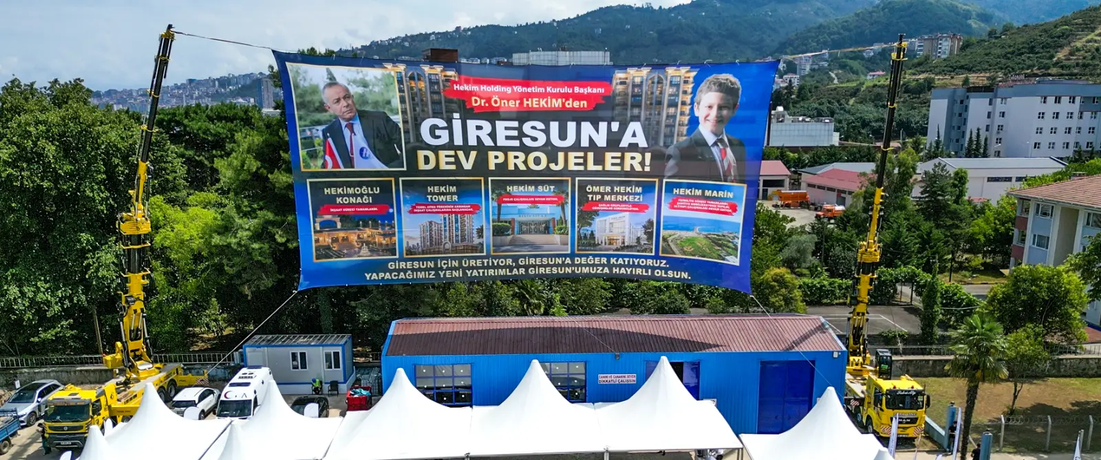 İki vinç arasına gerilmiş, Dr. Öner Hekim'in Giresun'a kazandıracağı beş projeyi tanıtan büyük branda; arka planda şehir ve yamaç manzarası